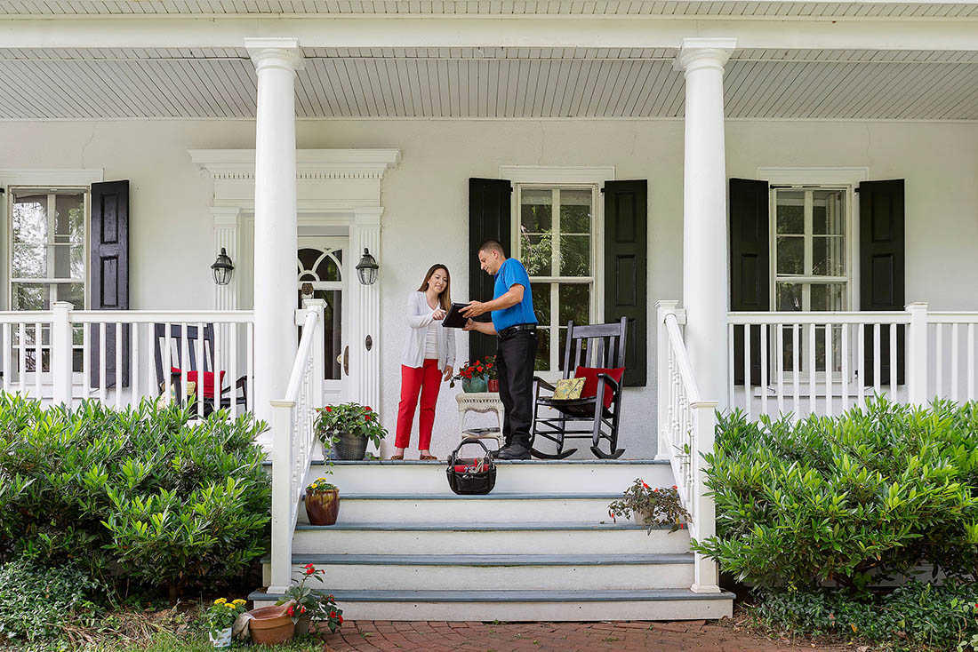 About Us Call Out Homeowner standing on front porch discussing HVAC service with a technician